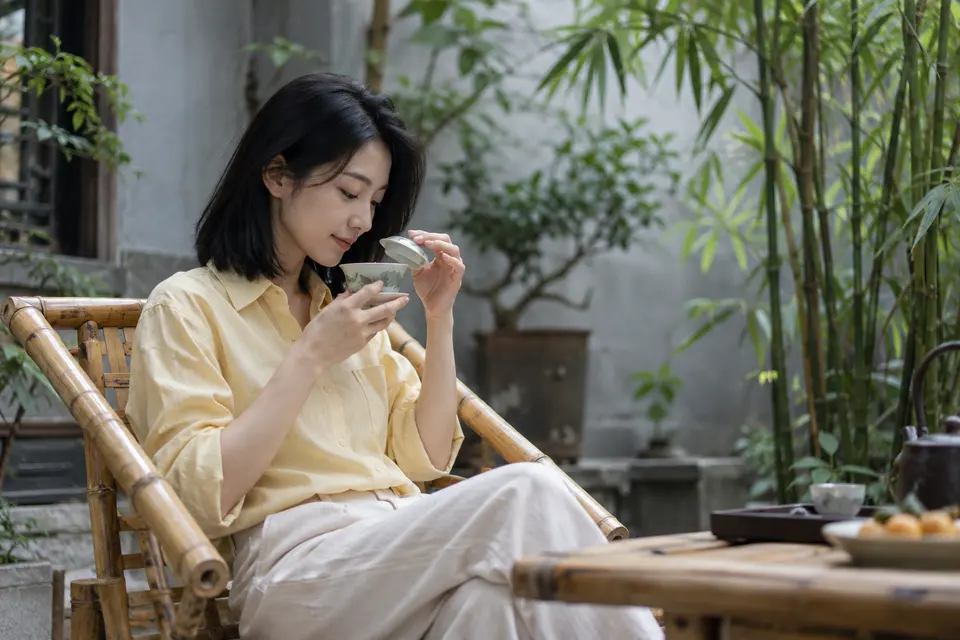 竹影院落里，一位年轻女性端起盖碗闻香的休闲画面